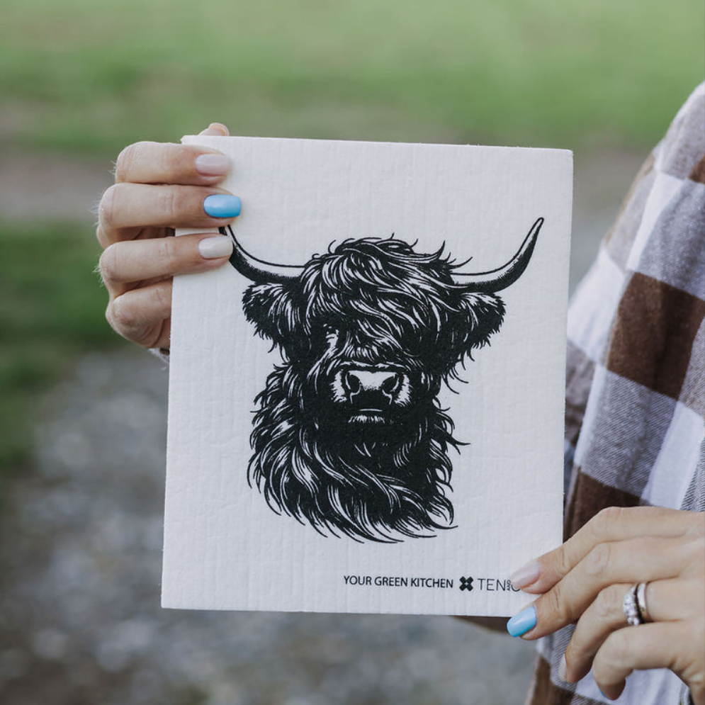 a person holding a reusable sponge cloth with a picture of a cow