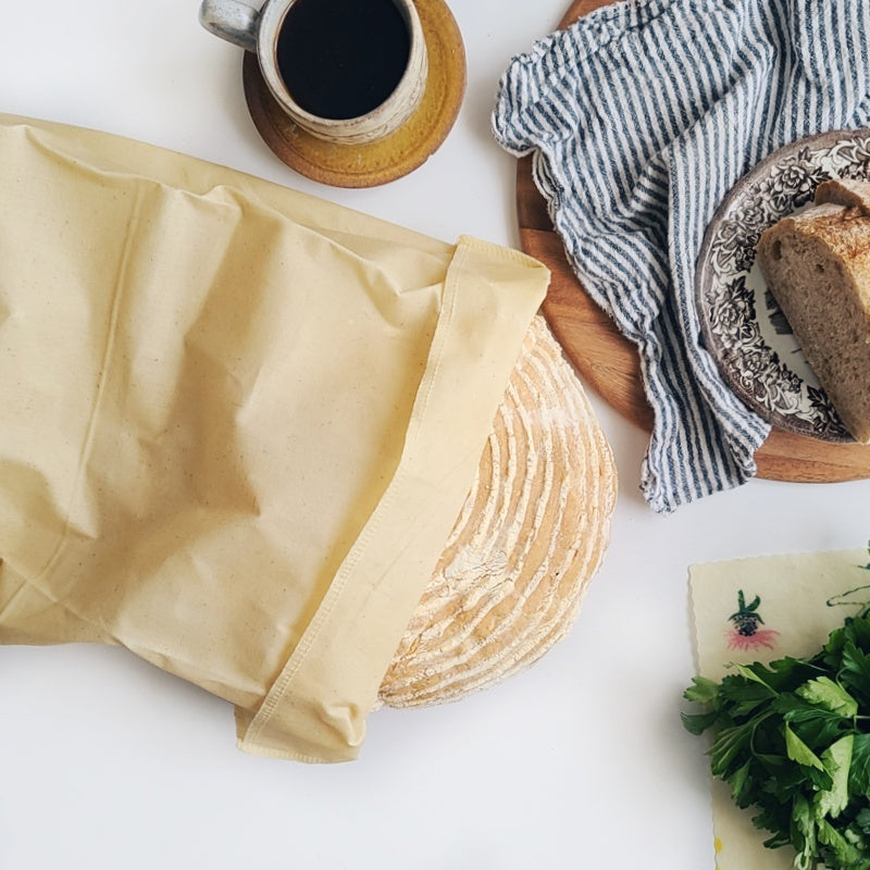 Bread in a beeswax bag, cup of coffee, and bread on a plate on a white surface