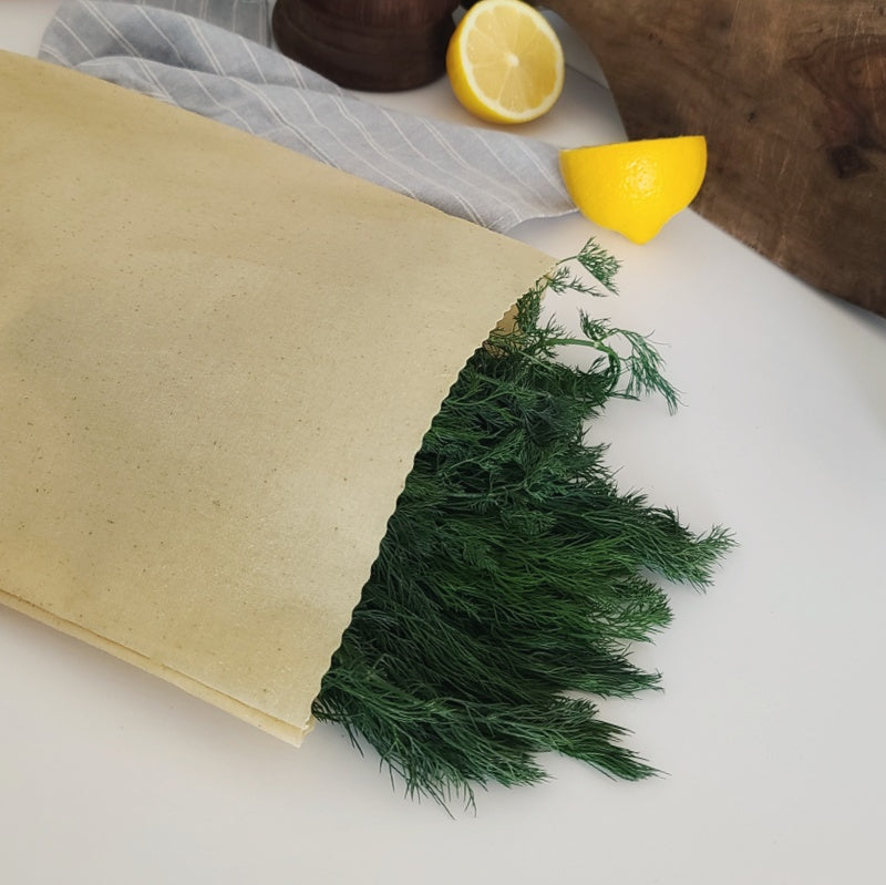 Green dill on a white surface with a lemon and wooden board in the background