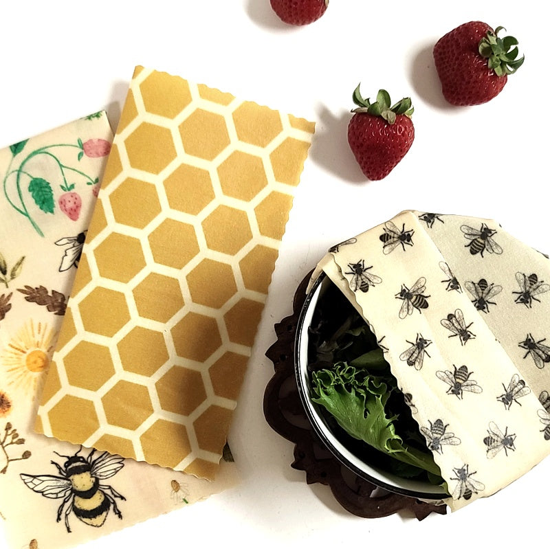 Reusable beeswax food wraps in a honey bee pattern, shown with a strawberry and leaves, indicating they are for food storage.